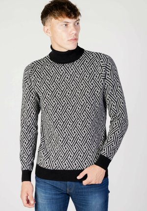 Maglione a collo alto a righe bianche e nere con maniche lunghe e polsini a coste, realizzato in un tessuto a maglia testurizzato, abbinato a jeans blu.