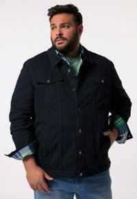 Tmavě modrá denimová bunda s kovovými knoflíky, náprsními kapsami a volným střihem. Pod ní se nachází kostkovaná košile s modrými a zelenými odstíny.