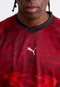 Rød sportstrøye med et teksturert mønster, med svart krage og en hvit Puma-logo på fronten.