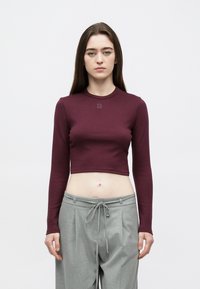 Burgundia pikkade varrukatega lühike top ümmarguse kaelusega ja tikitud "HUGO" logoga. Kombineeritud helehallide kõrge vöökohaga pükstega, millel on vööpael.