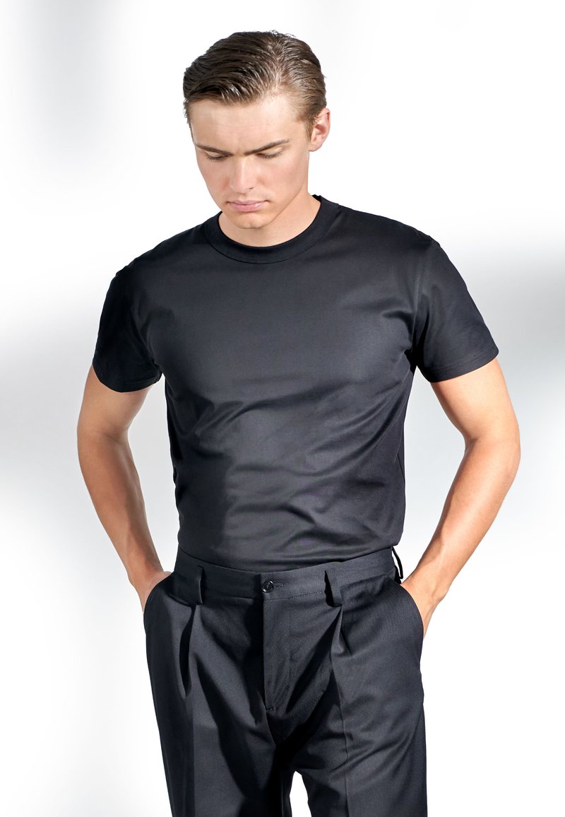 Svart t-shirt med rund hals i mjukt tyg, matchad med skräddarsydda svarta byxor med klassiska veck och sidofickor. En enkel, skräddarsydd look.