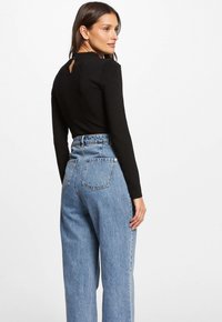 Top negro de manga larga con detalle de abertura en la parte posterior, combinado con pantalones vaqueros de tiro alto en azul claro y pierna amplia que tienen bolsillos traseros.