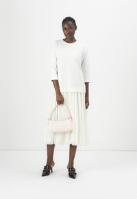 Maglione bianco a tre quarti, gonna plissettata color crema, mule nere con tacco e dettagli in fibbia, e borsa rosa chiaro con un design curvo.