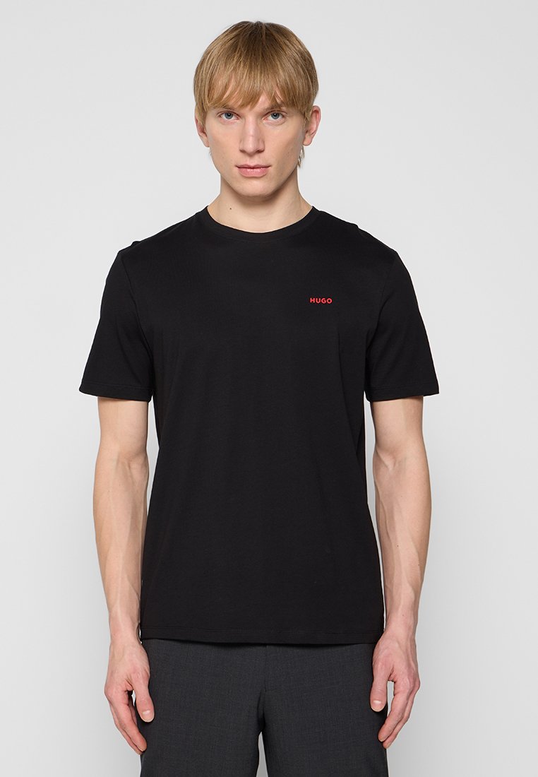 T-shirt en coton noir avec un col rond, des manches courtes et un petit logo rouge "HUGO" sur la poitrine. Texture lisse.