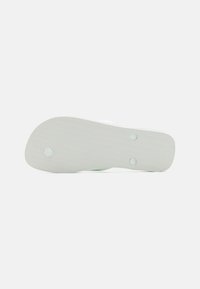 Vit gummiskosula med en strukturerad yta och två cirkulära hål. Designen har en rund form och ett minimalistiskt mönster.
