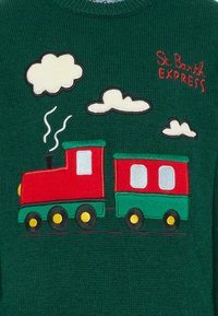 Czerwona i zielona zabawkowa lokomotywa parowa z kłębami dymu, trzy chmury oraz czerwony napis "St. Barth EXPRESS" na ciemnozielonym tle z tkaniny.