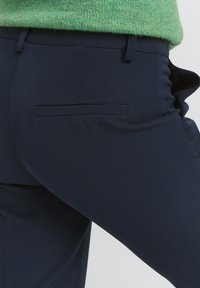 Granatowe spodnie o eleganckim fasonie i teksturowanej tkaninie. Posiadają jedną kieszeń z tyłu i płaski pas.