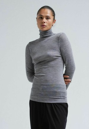 Grauer langärmeliger Rollkragenpullover aus einem weichen, strukturierten Stoff, mit einer figurbetonten Silhouette und subtilen horizontalen Streifen. Kombiniert mit schwarzen Hosen.