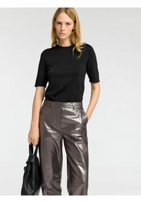 Musta lyhythihainen tekstuurinen neulepaita, joka on yhdistetty korkeavyötäröisiin kiiltäviin ruskeisiin nahkahousuihin, täydentää musta käsilaukku.