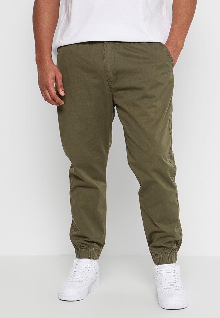 Pantaloni jogger a gamba affusolata verde oliva con vita e polsini elasticizzati, dotati di tasche laterali e in un morbido tessuto misto cotone. Abbinati a sneaker bianche.