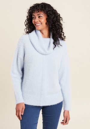 Pull léger bleu clair à col cowl, avec des manches longues, des poignets et un ourlet côtelés. Texture douce et coupe décontractée, associé à un jeans sombre.