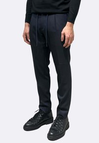 Pantaloni blu navy con design a pieghe, vita con coulisse e texture liscia abbinati a scarpe nere con lacci e occhielli metallici.