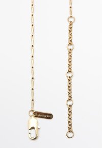 Gouden kettingaccessoire met langwerpige schakels en een kreeftsluiter. Beschikt over een merketiket en een extra cirkelvormige schakeldetail. Gladde textuur.
