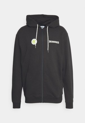 Schwarze Kapuzenjacke mit Reißverschluss aus weichem Stoff, mit einer Vorderasche, verstellbaren Kordeln, weißem Logo auf der Brust und grünem Badge.