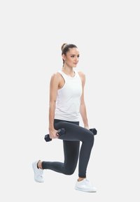 Valge toppi ja musti retuuse kandev naine teeb hõlpsalt raskustega kõhulihaseid, hoides käsipinke valge tausta ees.