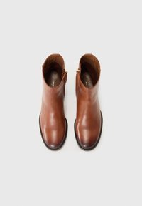 Bottines en cuir brun avec une finition lisse, des zips latéraux et un bout arrondi. Les semelles sont sombres avec un bord texturé.