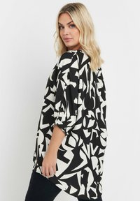 Tunica bianca e nera con motivi geometrici astratti, tessuto leggero, silhouette rilassata, maniche a tre quarti, dettagli arricciati ai polsini.