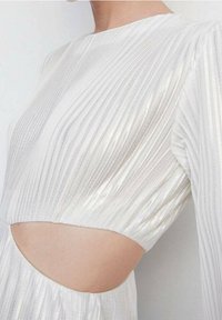 Robe blanche avec des plis verticaux, manches longues et une section médiane découpée. Fabriquée dans un tissu scintillant, avec une texture lisse qui met en valeur les courbes.