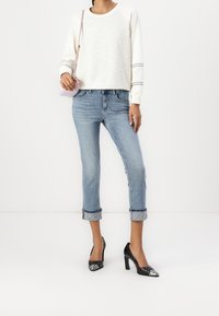 Valkoinen tekstuurinen huppari, vaaleansiniset lyhyet farkut, joissa on käännetyt lahkeet, ja mustat korkokengät hopeisilla yksityiskohdilla. Pieni vaaleanpunainen laukku.