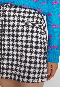 Zwart-wit houndstooth patroon rok met een ritsluiting, voorzien van een textuurstof en zijzakdetail.