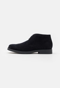 Bottines en daim noir avec un faible talon, un design à lacets et un bout légèrement arrondi. Texture lisse avec des détails de couture minimaux.