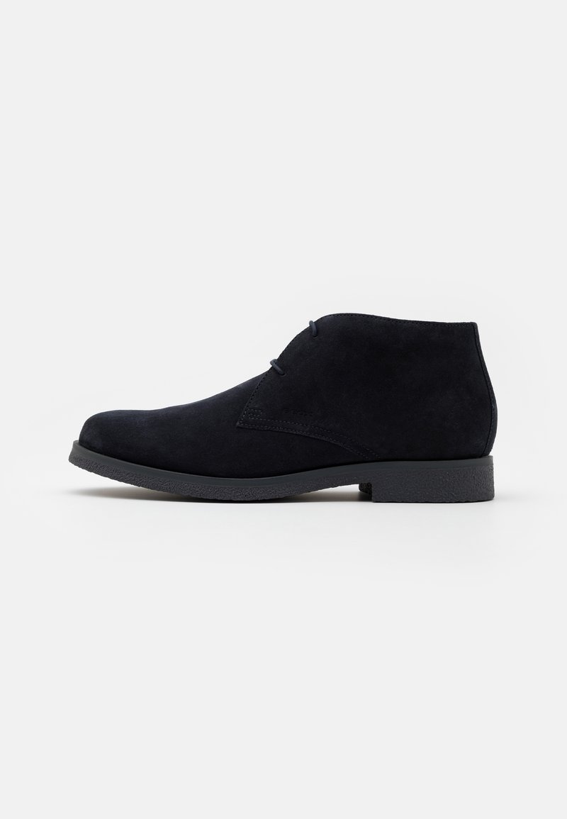 Bottines en daim noir avec un faible talon, un design à lacets et un bout légèrement arrondi. Texture lisse avec des détails de couture minimaux.