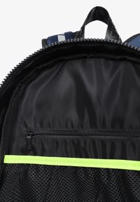 Interior de mochila de tela negra con un bolsillo con cremallera y una sección de malla. Presenta una franja de acento verde reflectante a lo largo de la parte inferior.