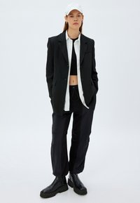 Schwarzes übergroßes Blazer, weißes Hemd, schwarzes Crop-Top, lockere schwarze Hose, schwarze Stiefeletten und weiße Mütze. Glattes Material, strukturierter Schnitt.