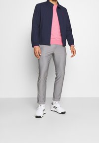 Giacca bomber navy, maglione rosa a girocollo, pantaloni grigi chiari e scarpe sportive bianche con dettagli neri. Design minimalista, texture liscia.