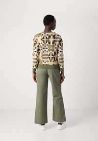 Pull en laine avec des motifs géométriques en crème, vert et marron ; associé à un pantalon large vert olive et des baskets blanches.