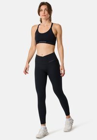 Black sports bra and high-waisted leggings made of stretchy fabric. Features a minimalistic design with logo accents on both pieces.