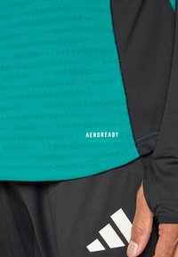 Turkio spalvos sportinis marškinėlis su tekstūruotu raštu, juodais akcentais ir „AEROREADY“ logo. Turi ilgus rankovus ir liekną dizainą.