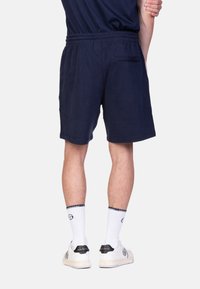 Shorts navy avec taille élastique, poche arrière et coupe droite. Portés avec des chaussettes blanches et des baskets arborant un logo noir.