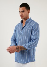 Camicia a maniche lunghe con bottoni di colore blu e righe verticali bianche. Tessuto testurizzato, colletto a punta e bottoni a contrasto.