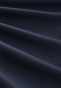 Tejido azul marino con una superficie lisa y ligeramente texturizada, que presenta caídas suaves y un brillo sutil a través de las capas plegadas.