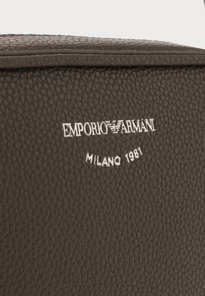 Тъмнокафява текстурирана кожена повърхност с бяло бродирано лого на Emporio Armani и текст "Milano 1981" под него.