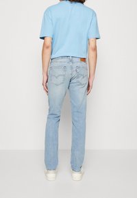 T-shirt en coton bleu clair à manches courtes, associé à un jean en denim clair avec des poches arrière et une étiquette en cuir près de la ceinture.