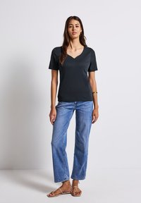 T-shirt noir à col en V avec des manches courtes, fabriqué en tissu lisse. Associé à un jean droit bleu et des sandales à lanières marron.