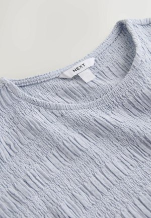Maglietta in tessuto azzurro chiaro con motivo arricciato elastico e scollo rotondo, con etichetta del marchio "NEXT" visibile sul colletto.