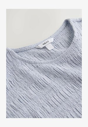 Maglietta in tessuto azzurro chiaro con motivo arricciato elastico e scollo rotondo, con etichetta del marchio "NEXT" visibile sul colletto.