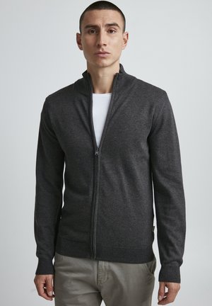 Mørk grå zip-up cardigan laget av mykt strikkemateriale. Har høy krage, lange ermer og ribbet mansjetter og kant.