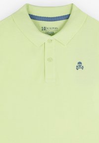 Polo en coton vert lime avec une patte de boutonnage à deux boutons, un col côtelé et un accent bleu à l'intérieur de l'encolure ; arbore un petit logo de crâne.