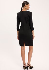 Czarna sukienka z rękawami trzyczwartkowymi, z suwakiem z tyłu, rozcięciem po boku i ozdobnymi guzikami na rękawach. Gładki materiał, dopasowany krój.