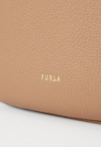 Beżowa torebka z teksturowanej skóry z wytłoczonym złotym logo "FURLA", o gładkim, zaokrąglonym kształcie i subtelnych wariacjach faktury.