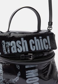 Geantă de mână neagră, lucioasă, cu o formă rotunjită. Are un mâner superior, curea ajustabilă și text imprimat în albastru deschis. Accente din metal.