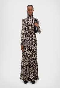 Robe à manches longues avec un motif ondulé noir et blanc, col haut, coupe ajustée, en tissu léger. Associée à un sac à main noir.
