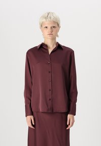 Bordová saténová košeľa s gombíkmi, golierom, dlhými rukávmi a predným zapínaním. Hladká textúra, mierne uvoľnený strih a viditeľná zodpovedajúca sukňa.