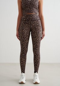 Treningsleggings med leopardmønster og høy midje, laget av elastisk stoff, kombinert med en matchende cropped topp og hvite joggesko.