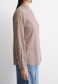 Beżowa koszula z długim rękawem, ozdobiona geometrycznym wzorem czerwonych i ciemno bordowych diamentów, z wysokim kołnierzem i zapięciem na guziki przy mankietach.