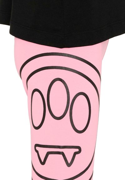 Crocs noirs et trois ovales verticaux dessinés en noir sur un tissu rose, avec un vêtement noir partiellement visible au-dessus.